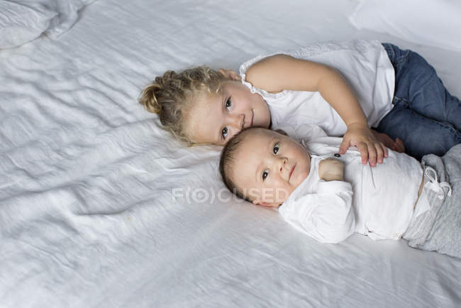 Маленькая девочка обнимается с младшим братом на кровати — стоковое фото