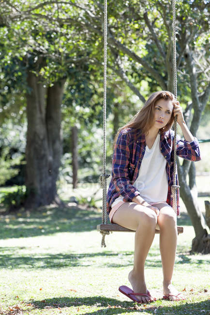 Mujer joven sentada en el parque columpio con expresión triste en la cara - foto de stock