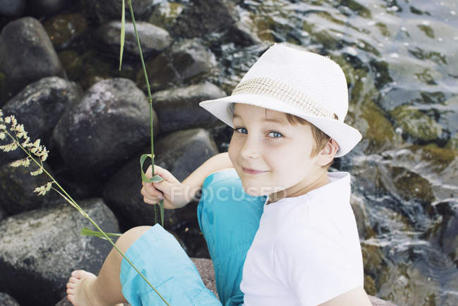 Niño usando sombrero sentado junto al arroyo - foto de stock