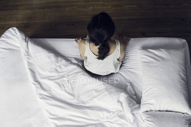 Vista aérea de la mujer sentada en el borde de la cama - foto de stock