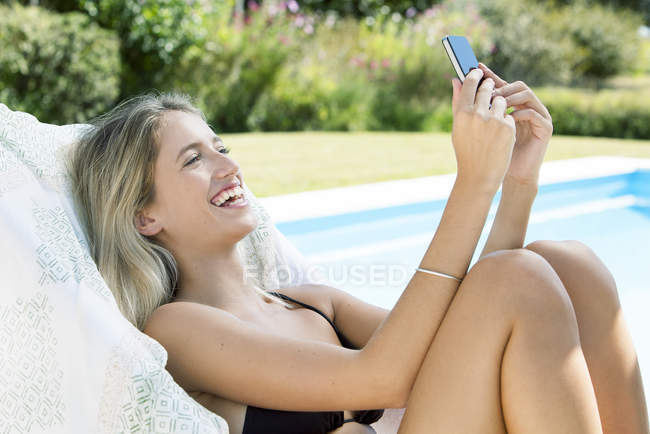 Женщина расслабляется у бассейна со смартфоном — стоковое фото