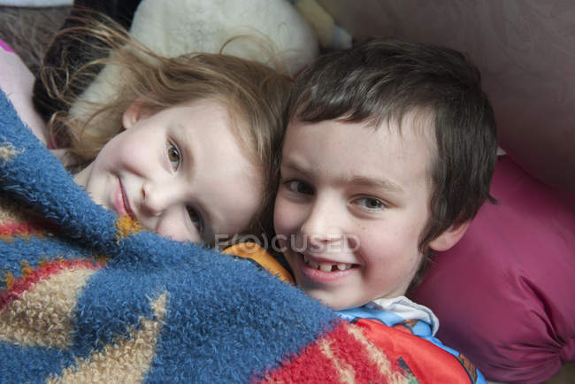 Portrait of young siblings lying under blanket together — Stock Photo