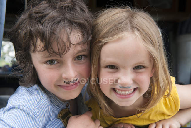 Retrato de hermanos jóvenes con el dibujo de bigotes falsos - foto de stock