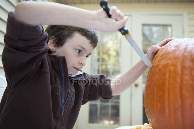 Мальчик вырезает тыкву ножом — стоковое фото
