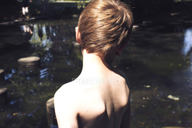 Vista trasera del niño con el pecho desnudo parado junto al agua - foto de stock
