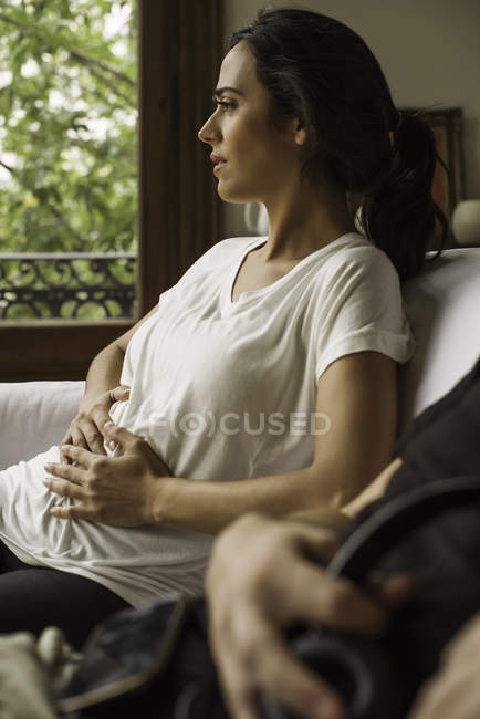Беременная женщина думает о своем личном будущем, сидя на диване с мужем — стоковое фото
