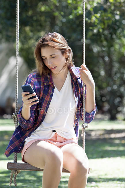 Молода жінка, сидячи на гойдалки, дивлячись на смартфон — стокове фото