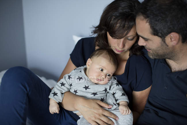Parents avec bébé garçon assis sur le lit à la maison — Photo de stock