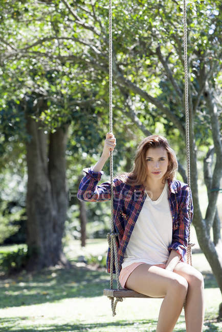 Portrait de jeune femme assise sur balançoire dans le parc — Photo de stock