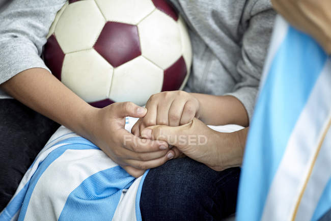 Vue recadrée de l'enfant et de l'adulte tenant la main et du ballon de football — Photo de stock