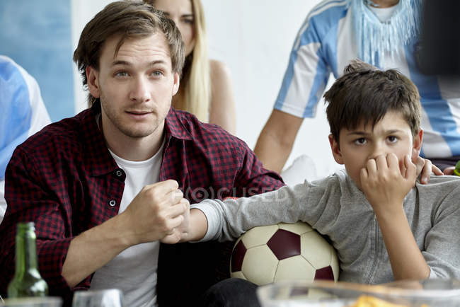 Père et fils se tiennent la main en regardant le match de football à la maison — Photo de stock