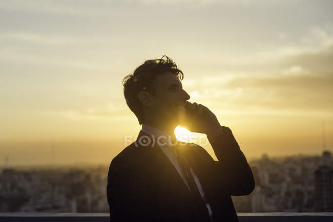 Человек разговаривает по мобильному телефону, освещенный закатом солнца — стоковое фото