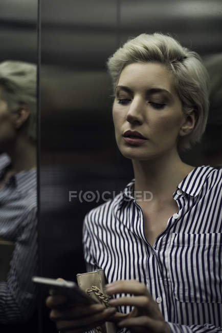 Woman using smart phone in elevator — Stock Photo