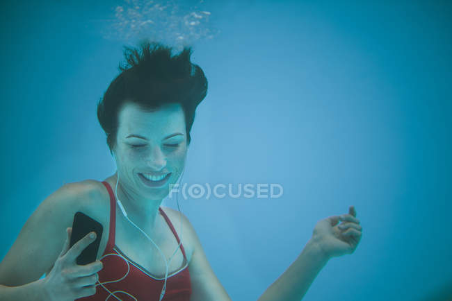 Woman listening to music with smartphone underwater — Stock Photo