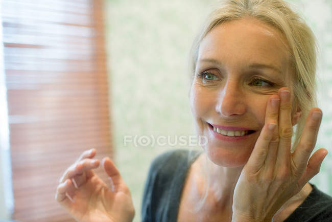 Femme mûre regardant son reflet dans un miroir avec les mains sur les joues — Photo de stock