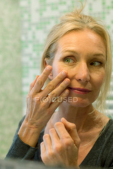 Femme mûre scrutant son visage dans le miroir de salle de bain — Photo de stock
