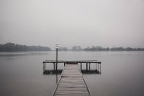 Деревянный пирс и озеро при туманном дневном свете — стоковое фото