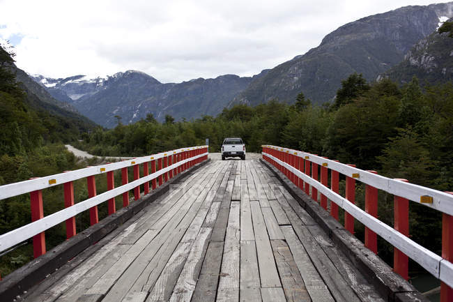 Vue arrière de la voiture conduite par pont en bois, paysage de montagnes en arrière-plan — Photo de stock