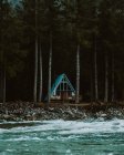 Vista diurna da cabana de madeira do triângulo na floresta na costa do rio — Fotografia de Stock
