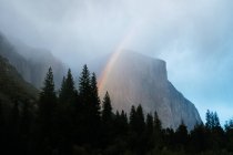 Vista diurna do arco-íris em nuvens sobre montanhas e florestas em Yosemite Valley, Califórnia — Fotografia de Stock