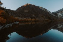 Montañas y árboles reflejados en aguas tranquilas del lago - foto de stock