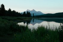 Vista distante delle montagne e della foresta riflessa in acque calme del lago — Foto stock