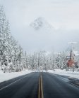 Vue de jour de la route de montagne avec forêt enneigée et maisons, col Snoqualmie, chaîne des Cascades, Washington — Photo de stock