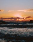 Vista à distância do pôr-do-sol colorido e paisagem marinha com ondas na praia — Fotografia de Stock