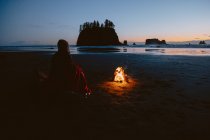 Portrait arrière d'une femme assise sur une plage de sable près d'un feu de joie au coucher du soleil. Second Beach, Péninsule Olympique, La Push, Washington — Photo de stock