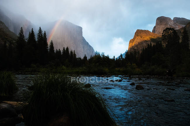 Vista diurna dell'arcobaleno nelle nuvole sulle montagne e sulla foresta nella Yosemite Valley, California — Foto stock