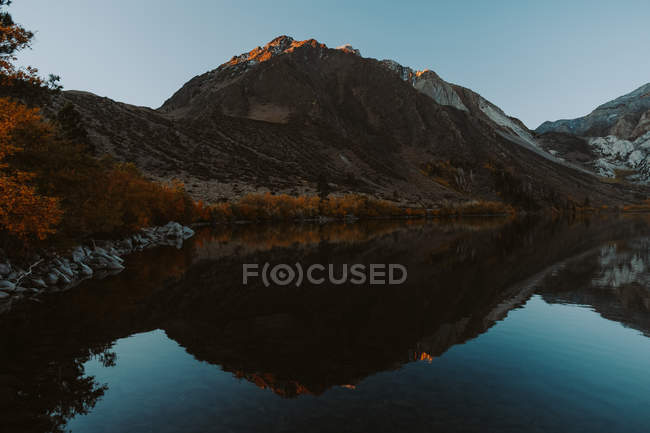 Mountains and trees reflected in calm lake water — Stock Photo