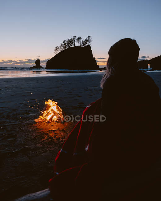 Portrait arrière d'une femme assise sur une plage de sable près d'un feu de joie au coucher du soleil. Second Beach, Péninsule Olympique, La Push, Washington — Photo de stock