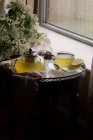 Té de miel de limón de jengibre en la tetera y en la taza en la mesa pequeña - foto de stock