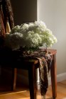 Fresh cut hydrangea flowers in wire basket on wooden chair — Stock Photo