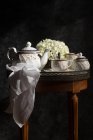 Tea-service and fresh flowers on small vintage table — Stock Photo