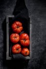 Tomates vermelhos maduros frescos em tecido preto em caixa — Fotografia de Stock