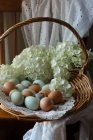 Huevos de colores en cesta con flores frescas cortadas - foto de stock
