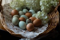 Huevos de colores en cesta con flores frescas cortadas - foto de stock