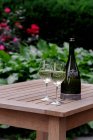 Склянки і пляшка білого вина на дерев'яному садовому столі — стокове фото