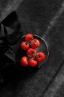 Pomodori rossi freschi su piatto su superficie nera — Foto stock