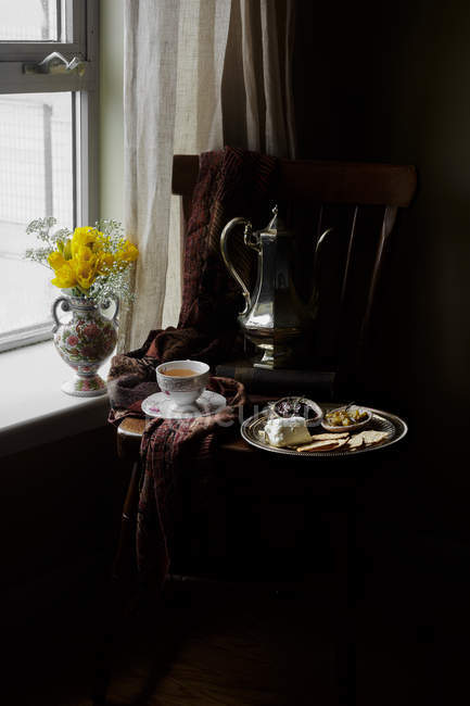 Сирна тарілка з крекерами та чатні на стільці з чашкою чаю та старовинним чайником — стокове фото