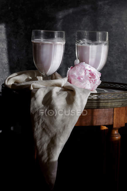 Leche de anacardo en vasos sobre una pequeña mesa de madera con flor y tela - foto de stock
