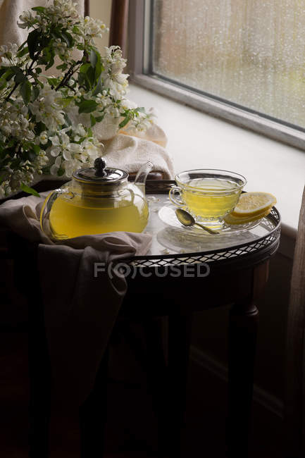 Имбирный лимонный мёд чай в чайнике и в чашке на маленьком столе — стоковое фото