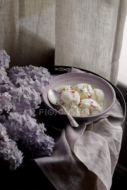 Fruit ice cream in bowl with purple lilac flowers — Stock Photo