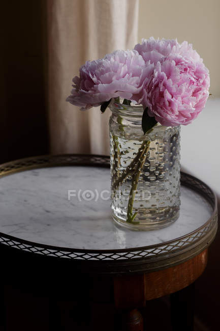 Свежевырезанные розовые пионы в банке на маленьком столе — стоковое фото