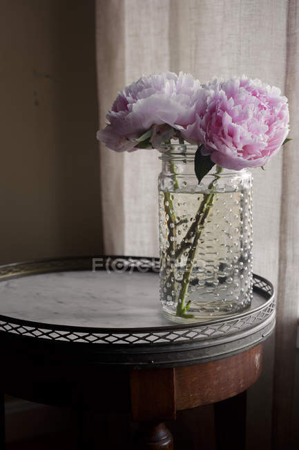 Frisch geschnittene rosa Pfingstrosen im Glas auf kleinem Tisch — Stockfoto