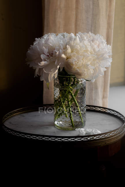 Fresh cut white peonies in jar on small table — Stock Photo