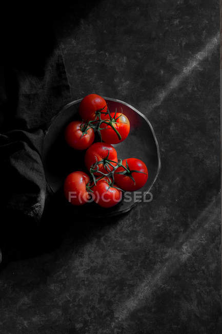 Fresh red tomatoes on plate on black surface — Stock Photo