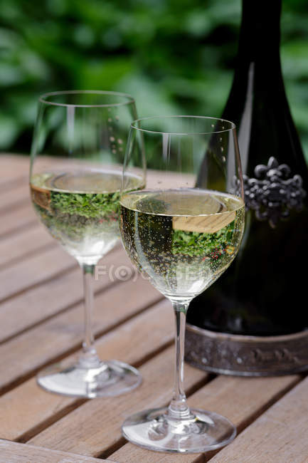 Copos e garrafa de vinho branco na mesa de jardim de madeira — Fotografia de Stock
