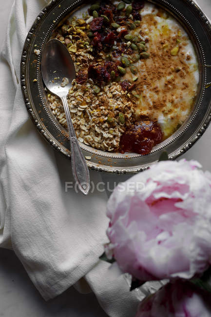 Tazón de yogur con avena y semillas en la mesa con peonías - foto de stock
